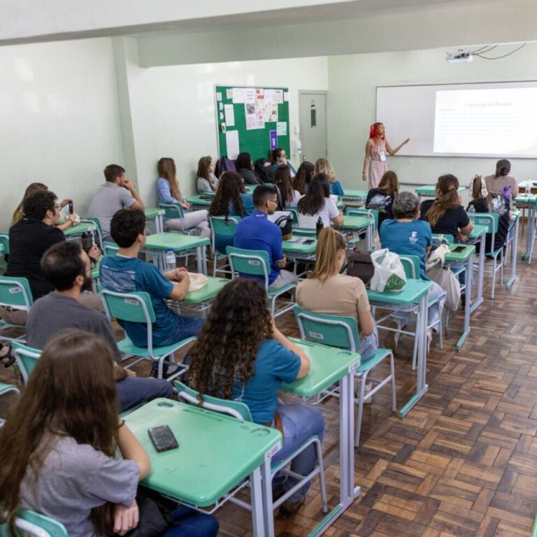 Estudantes assistem a apresentação de trabalhos em uma sala de aula.